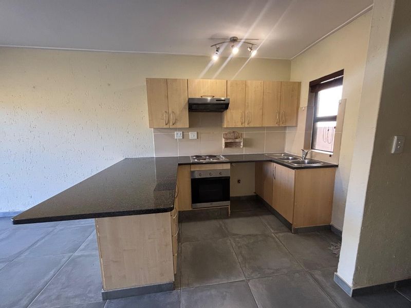 A functional kitchen featuring granite countertops, built-in cabinetry, an electric hob, oven, and extractor fan, with tiled flooring and a tiled backsplash.