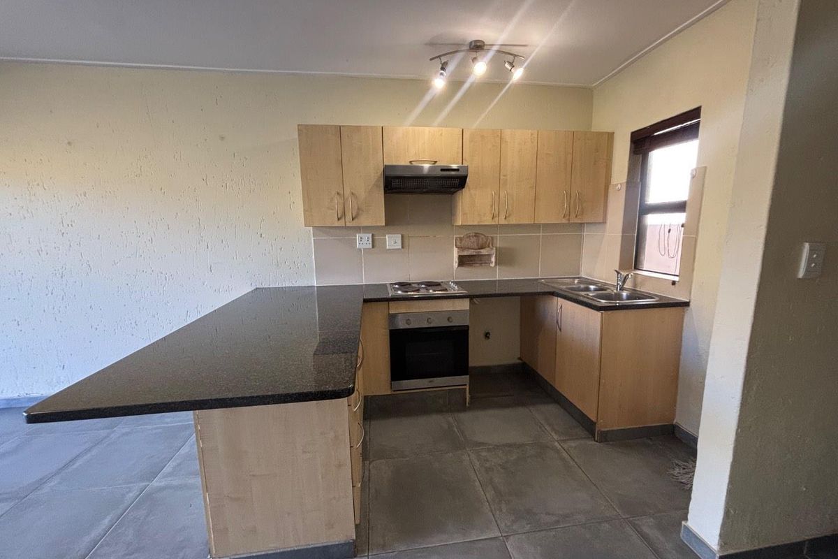 A functional kitchen featuring granite countertops, built-in cabinetry, an electric hob, oven, and extractor fan, with tiled flooring and a tiled backsplash.