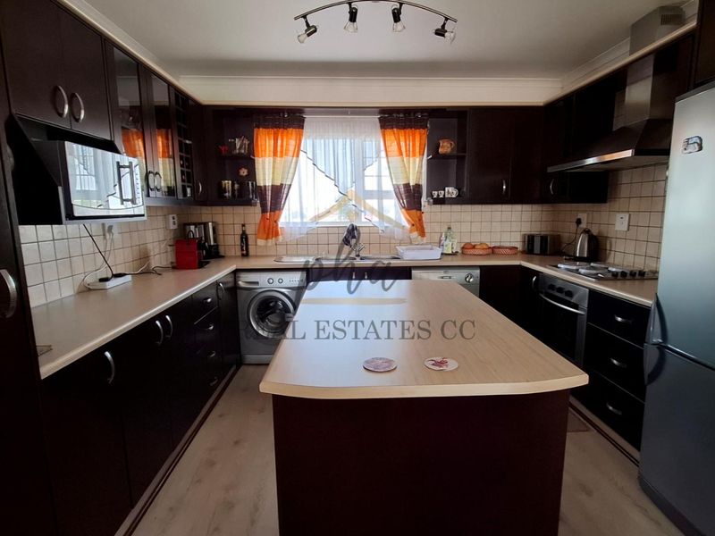 A functional kitchen featuring dark wood cabinetry, a central island, tiled backsplash, and integrated appliances, offering ample storage and workspace.