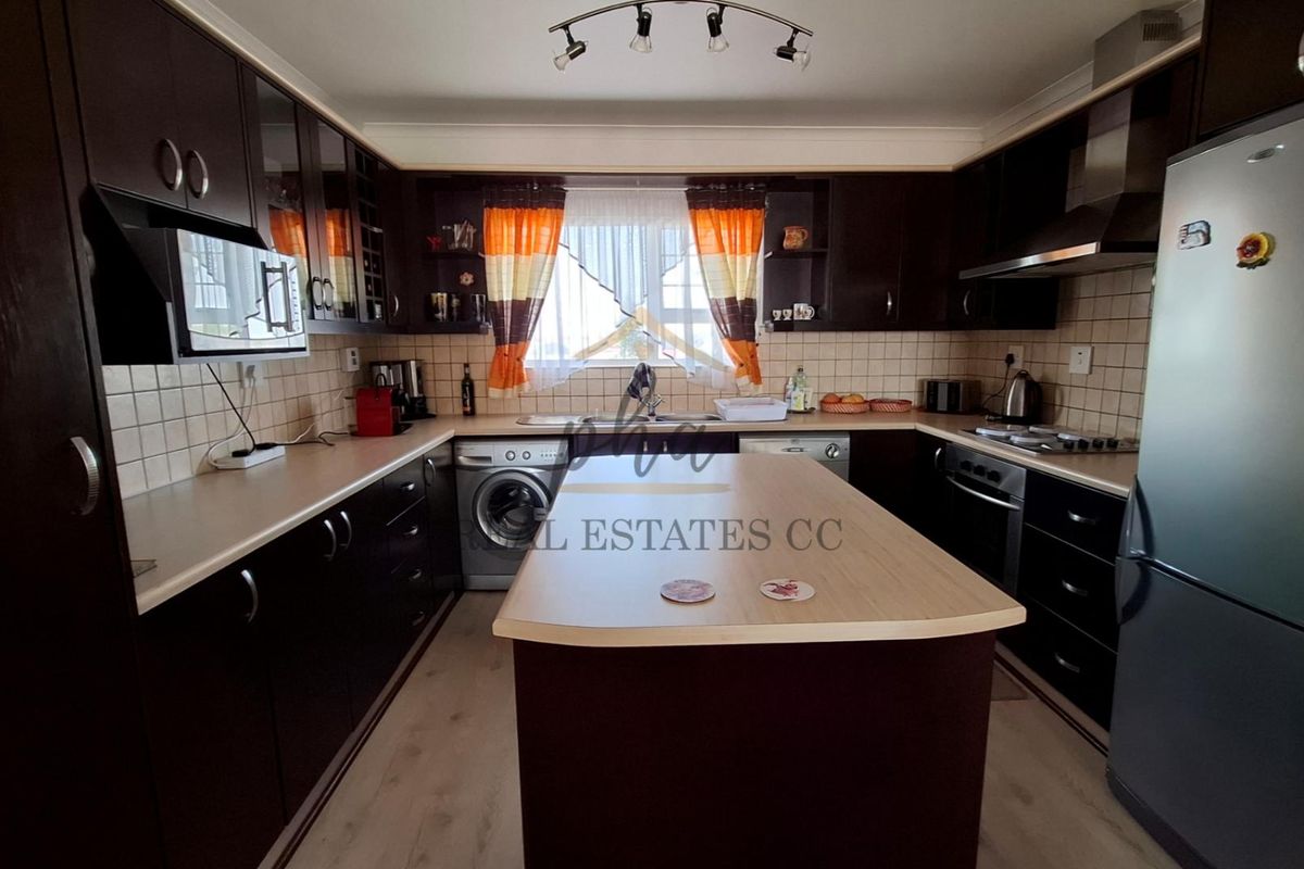A functional kitchen featuring dark wood cabinetry, a central island, tiled backsplash, and integrated appliances, offering ample storage and workspace.