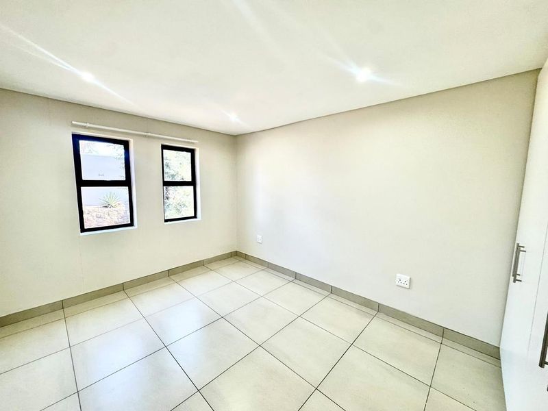 A bright, empty bedroom featuring neutral tiled flooring, recessed downlights, and a built-in cupboard with modern aluminium-framed windows.
