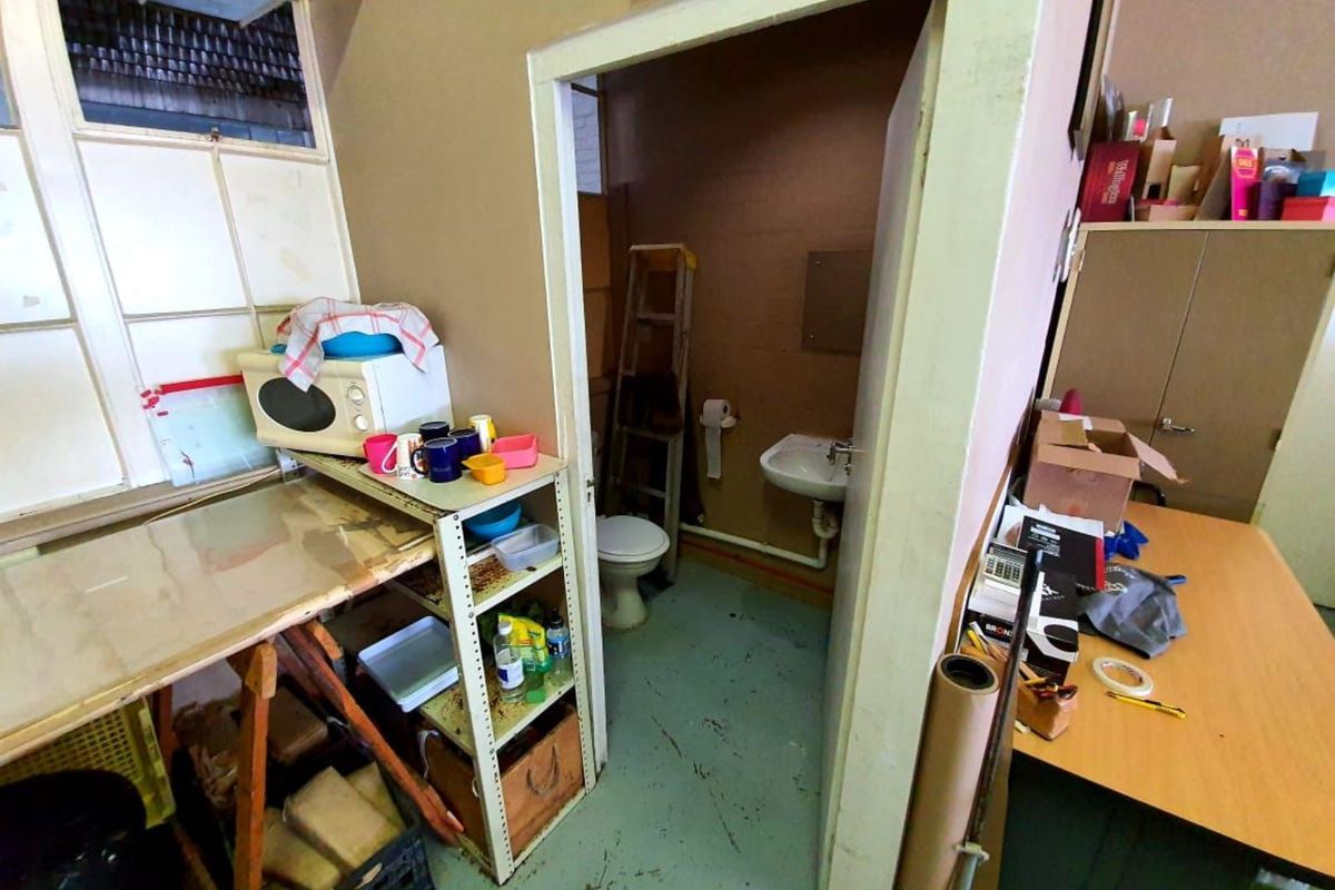 A small, dated bathroom facility featuring a basic toilet and wall-mounted basin, requiring significant maintenance and cosmetic updates.