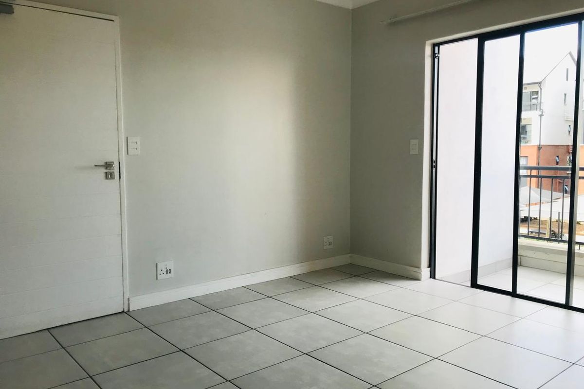 A bright, empty bedroom featuring neutral tiled flooring, a modern interior door, and large sliding glass doors providing access to a private balcony.