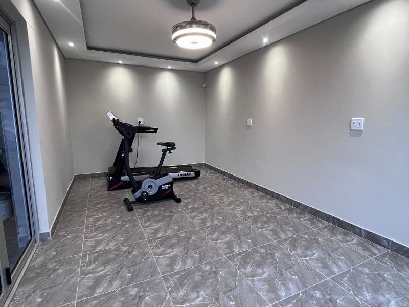 A modern, well-lit gym space featuring contemporary grey marble-look floor tiles, recessed ceiling lighting, and a central ceiling fan.