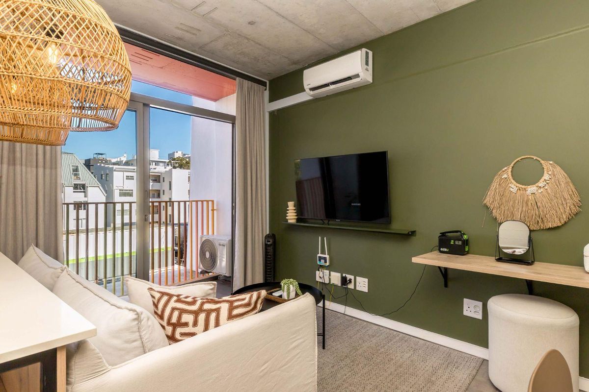 Modern living area featuring an exposed concrete ceiling, wall-mounted air conditioning unit, and sliding glass doors leading to a private balcony.