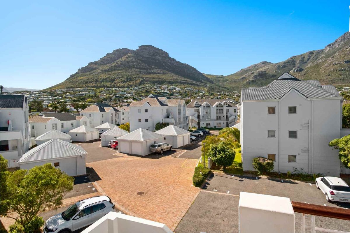 An elevated aerial view of an apartment complex featuring paved parking areas, white building facades, and a scenic mountain backdrop.