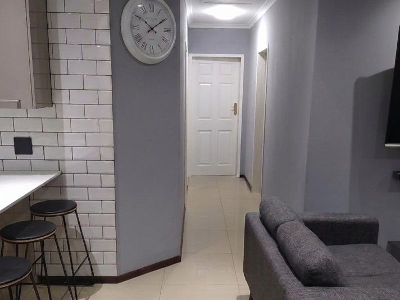 An open-plan living area featuring modern grey walls, a subway tile kitchen backsplash, tiled flooring, and recessed lighting leading to a hallway.