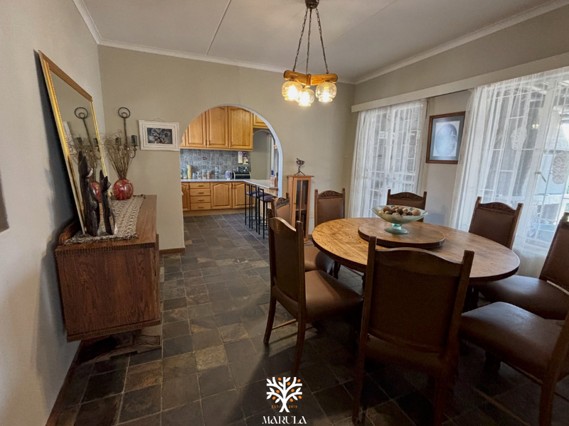 Open plan dining area featuring slate tile flooring and a classic archway leading into a functional kitchen with wooden cabinetry.