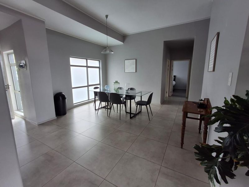 A bright and spacious dining area featuring neutral tiled flooring, modern recessed ceiling lighting, and large windows allowing for ample natural light.