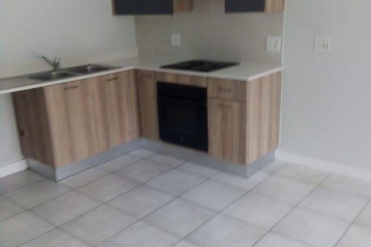 A modern kitchen featuring light wood-grain cabinetry, dark upper cabinets, a built-in oven, hob, extractor fan, and tiled flooring.