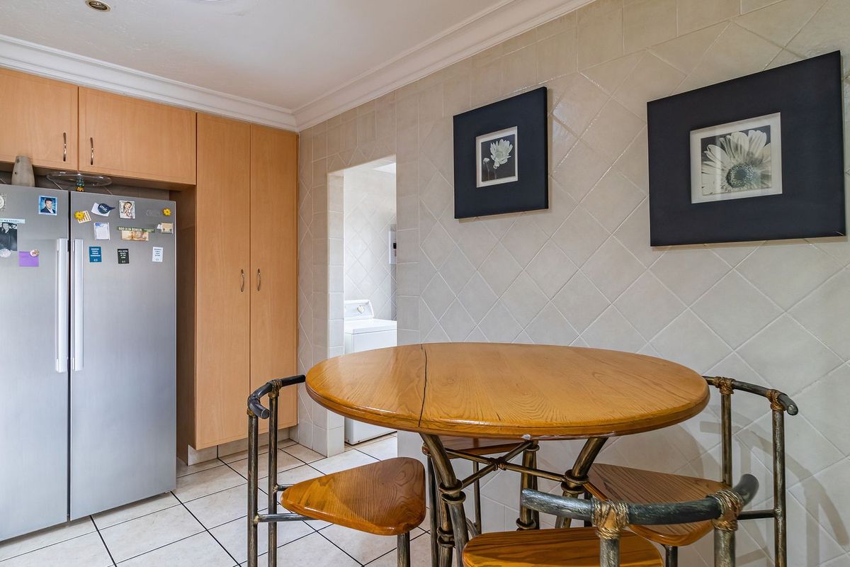 A functional kitchen area featuring light wood cabinetry, tiled walls, and tiled flooring, with a convenient adjacent laundry space visible.