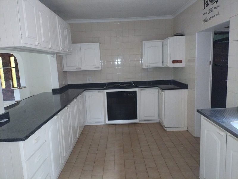 A functional kitchen featuring white built-in cabinetry, dark granite countertops, a built-in oven, and a gas hob with tiled splashbacks.