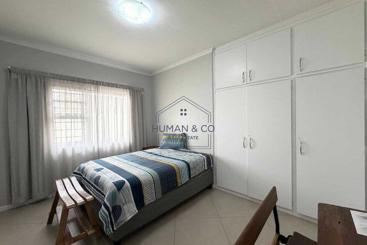A well-maintained bedroom featuring neutral tiled flooring, ample built-in cupboard storage, and natural light through a window with curtain rails.