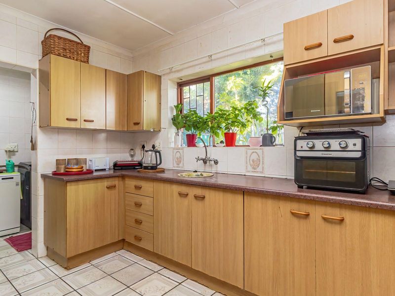 A functional kitchen featuring light wood-look cabinetry, laminate countertops, tiled backsplash, and tiled flooring, offering a practical layout with ample storage space.
