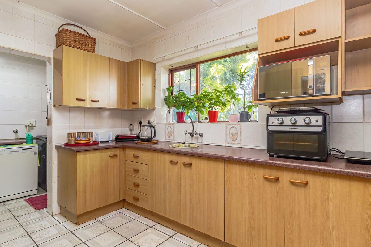 A functional kitchen featuring light wood-look cabinetry, laminate countertops, tiled backsplash, and tiled flooring, offering a practical layout with ample storage space.