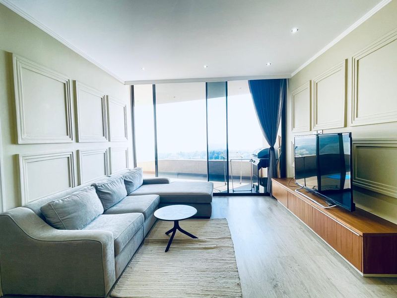 Modern living room featuring elegant wall molding, laminate flooring, recessed lighting, and large sliding glass doors opening to a balcony with scenic views.
