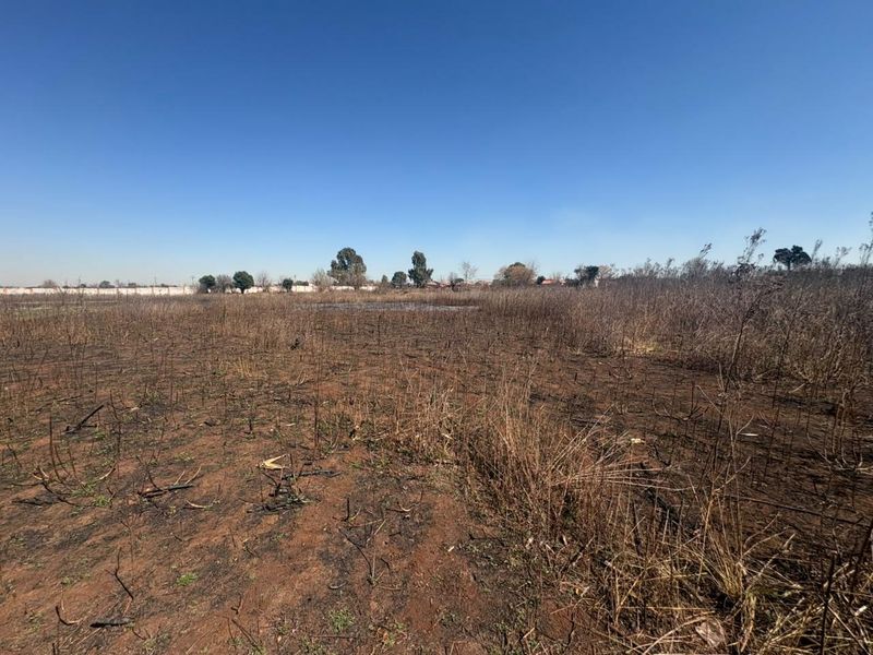 A wide-angle view of a vacant residential plot featuring dry, scorched vegetation and open land.