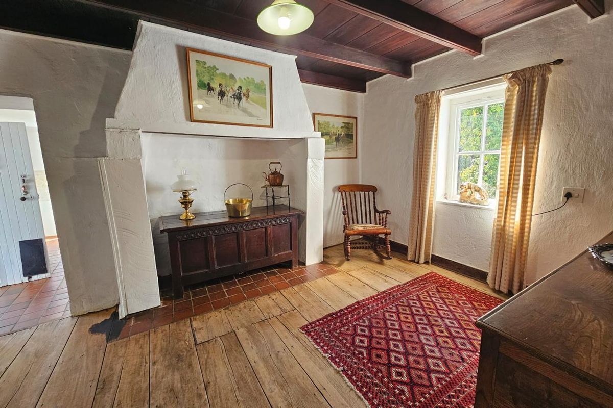 A rustic living room featuring exposed timber ceiling beams, a traditional masonry fireplace, and original wide-plank wooden flooring.