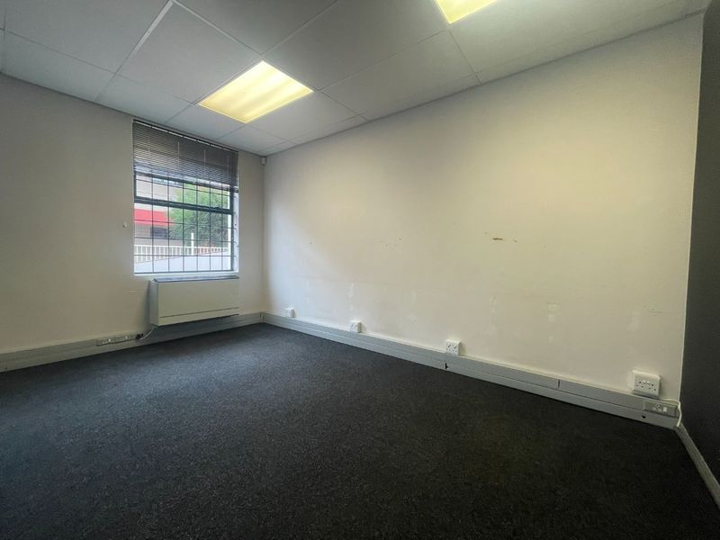 A vacant office space featuring carpeted flooring, a suspended ceiling with recessed lighting, and a wall-mounted HVAC unit.