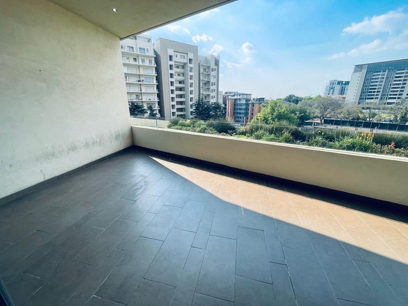 A spacious covered balcony featuring tiled flooring, a modern glass balustrade, and elevated urban views, offering a versatile outdoor living space.