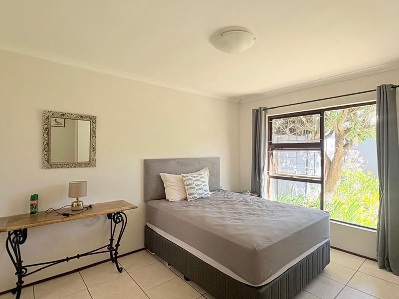 A well-lit bedroom featuring tiled flooring, a large window with garden views, and built-in wardrobe storage.