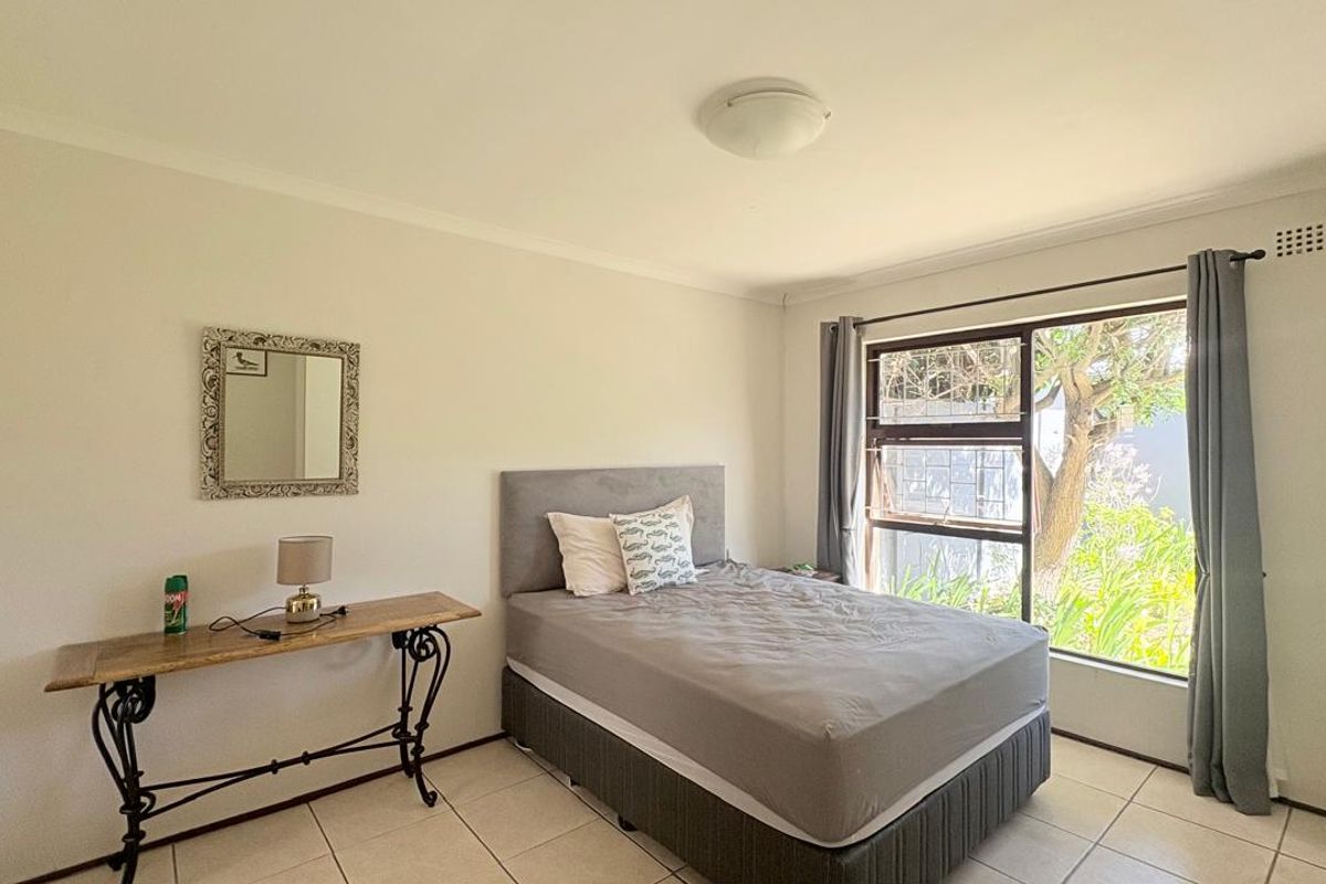 A well-lit bedroom featuring tiled flooring, a large window with garden views, and built-in wardrobe storage.