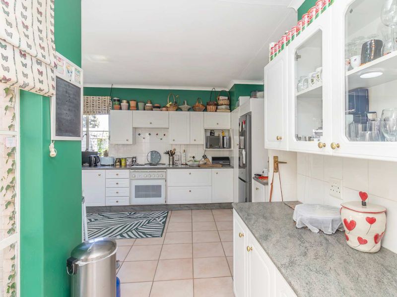 A functional kitchen featuring white cabinetry, stone countertops, tiled flooring, and a built-in oven with hob, offering a bright and practical workspace.