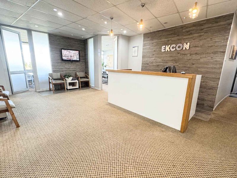 Professional office reception area featuring a modern built-in desk, wood-look feature wall, glass partitions, and a clean, well-lit waiting space.