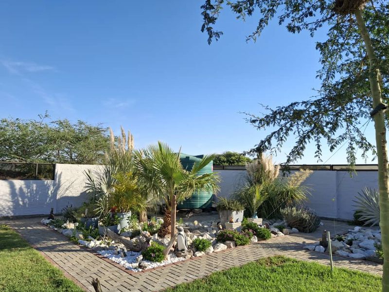 A well-maintained garden area featuring paved walkways, established landscaping, and a large water storage tank enclosed by a boundary wall.