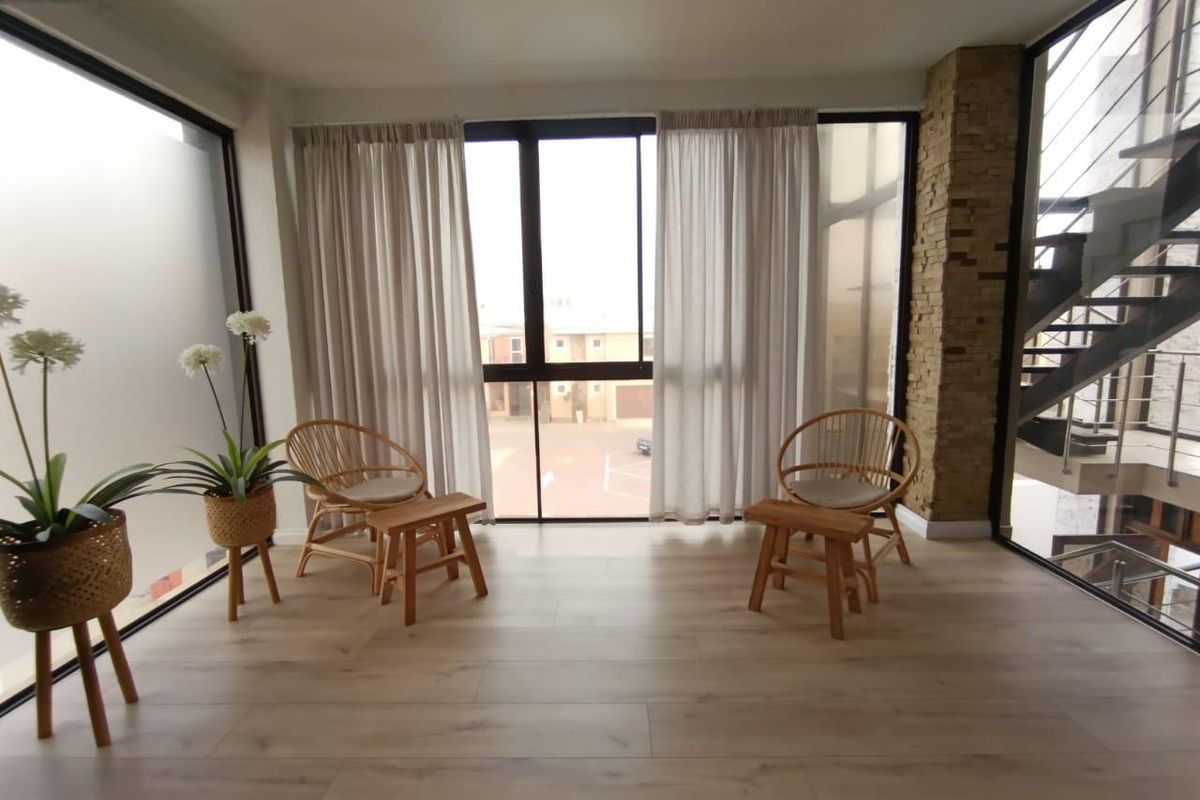 A bright living area featuring modern laminate flooring, a stone-clad feature wall, and large windows providing ample natural light and a view of the exterior.