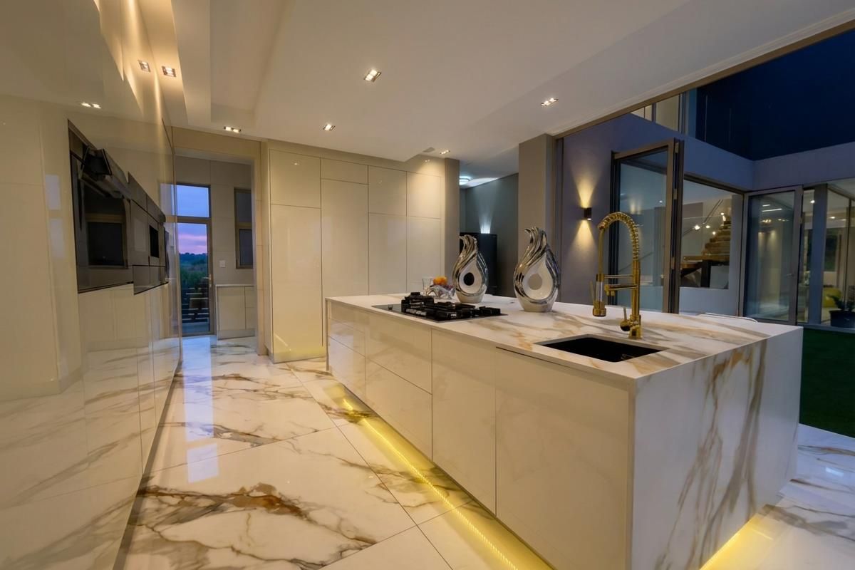 Modern kitchen featuring a large marble-topped island with integrated gas hob, gold-tone faucet, high-gloss cabinetry, and recessed LED lighting.