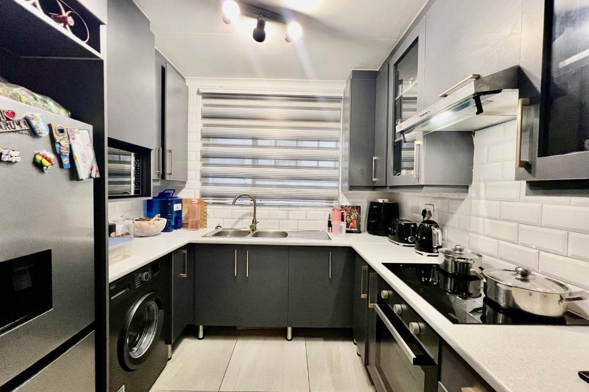Modern kitchen featuring dark grey cabinetry, white subway tile backsplash, integrated oven, hob, extractor fan, and a double sink with brass faucet.