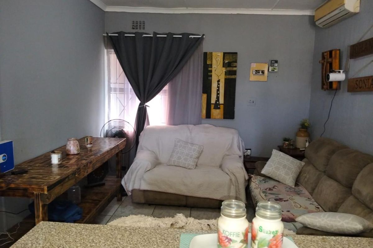 A cozy living room area featuring tiled flooring, an integrated air conditioning unit, and window security bars.