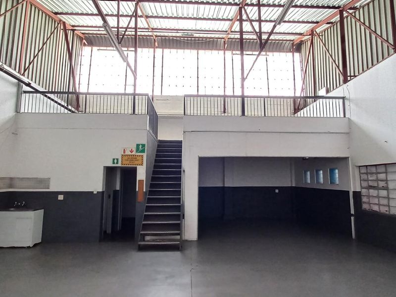 Spacious industrial utility area featuring a mezzanine level, metal staircase, exposed roof trusses, and durable flooring, suitable for warehouse or workshop use.