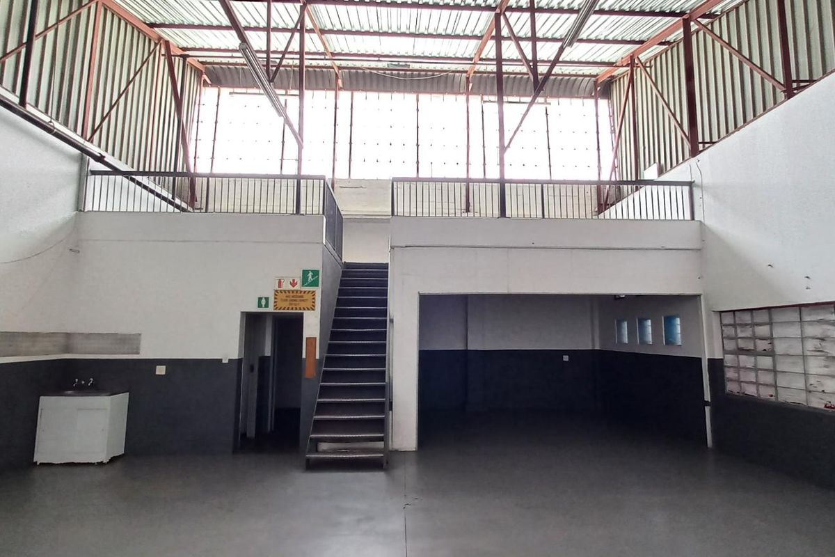 Spacious industrial utility area featuring a mezzanine level, metal staircase, exposed roof trusses, and durable flooring, suitable for warehouse or workshop use.