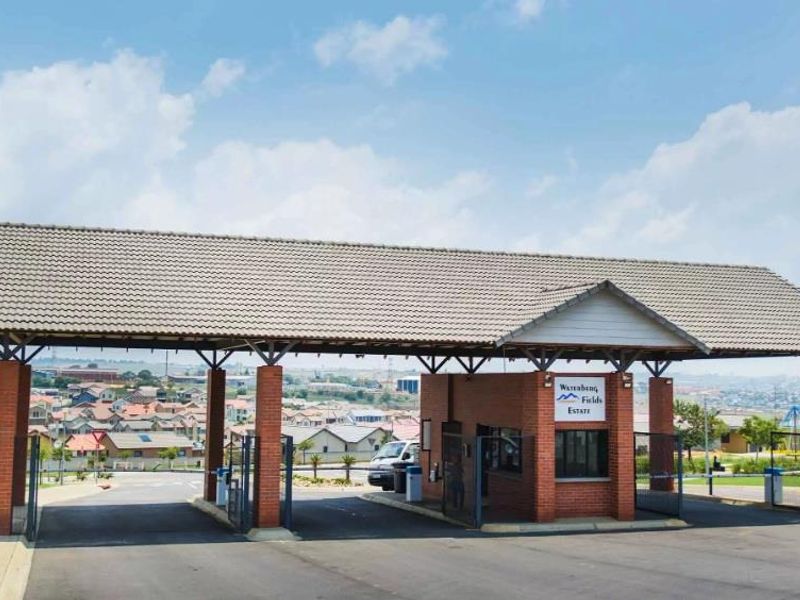 The main entrance gatehouse of Waterberg Fields Estate, featuring a brick structure, tiled roof, and secure access control points.