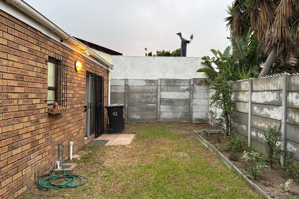 A private rear garden featuring a brick exterior wall, precast concrete boundary fencing, and a small landscaped garden bed.