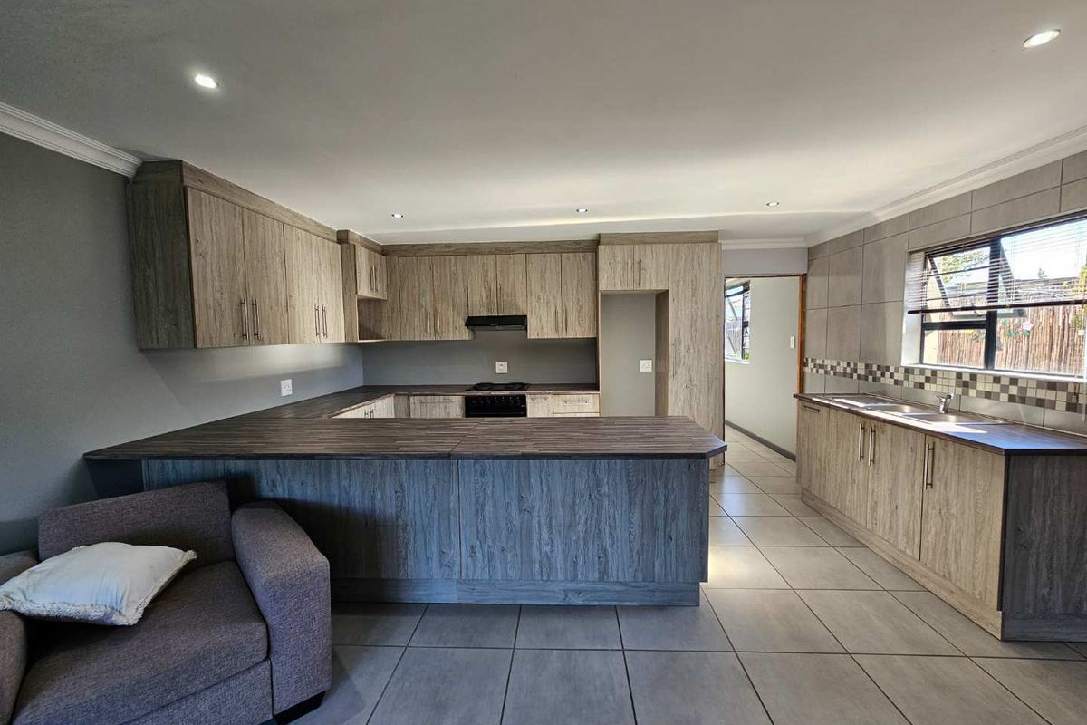 Modern open-plan kitchen featuring wood-grain cabinetry, laminate countertops, integrated appliances, tiled backsplash, and recessed lighting.