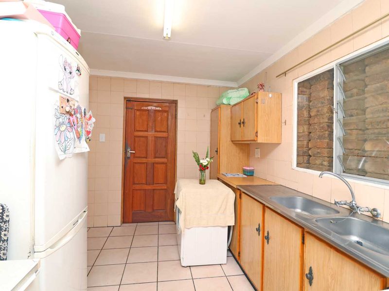 A functional kitchen featuring tiled walls and flooring, wooden cabinetry, and a double stainless steel sink with a louvered window.