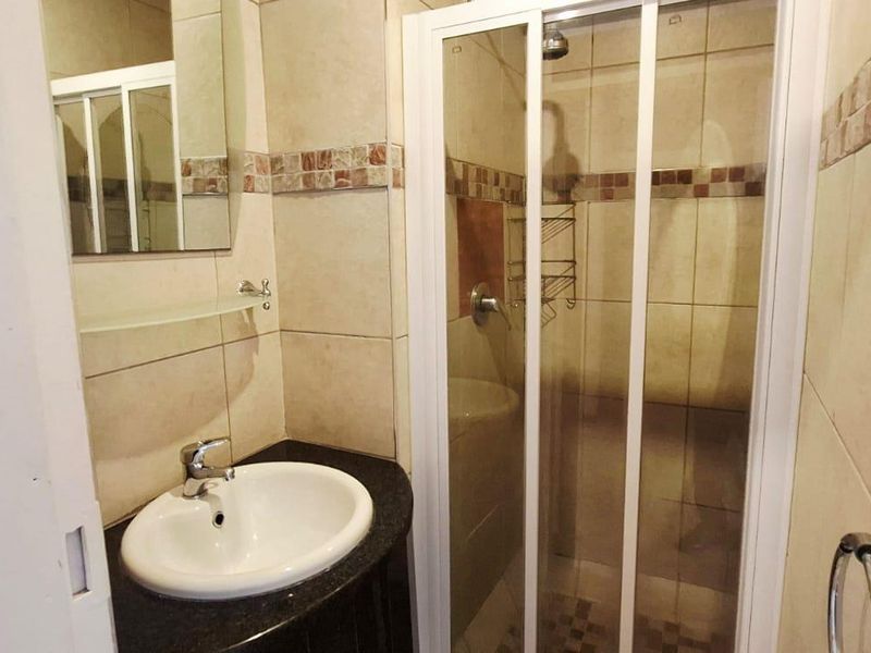 A functional bathroom featuring a vanity basin, a shower enclosure with a glass door, and neutral wall tiling.