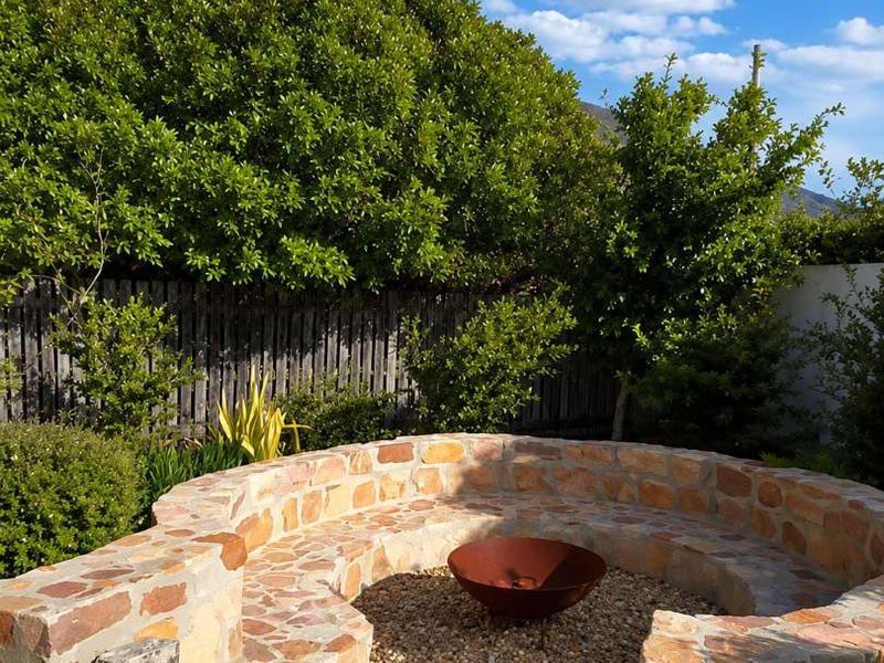 A well-maintained garden area featuring a circular stone-clad seating structure with a central fire pit and gravel landscaping.
