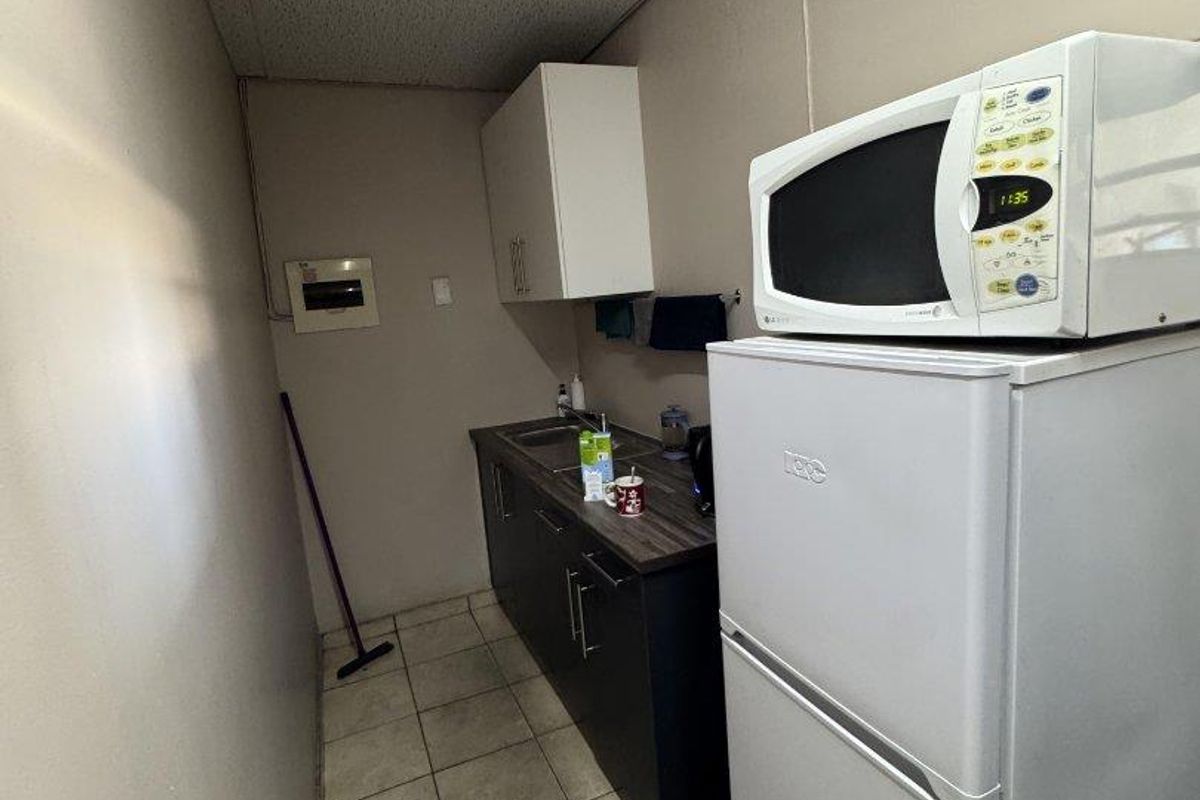 A compact industrial kitchenette featuring dark base cabinetry, a stainless steel sink, tiled flooring, and a drop ceiling.