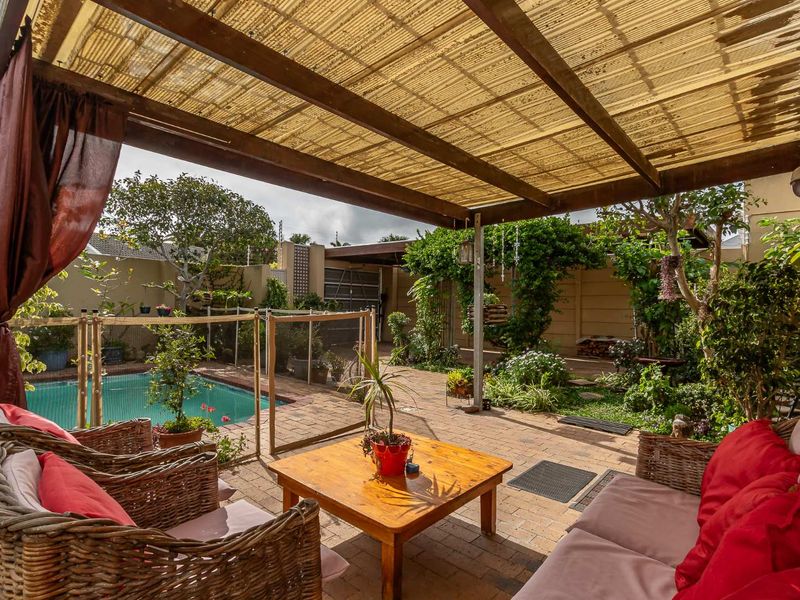 Covered outdoor patio area featuring a timber pergola with translucent roofing, brick paving, and direct access to a private swimming pool and garden.