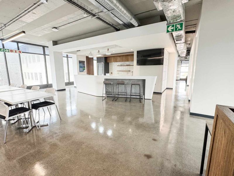 Modern open-plan office space featuring polished concrete floors, exposed industrial ceiling ductwork, and a sleek built-in kitchen area with contemporary finishes.
