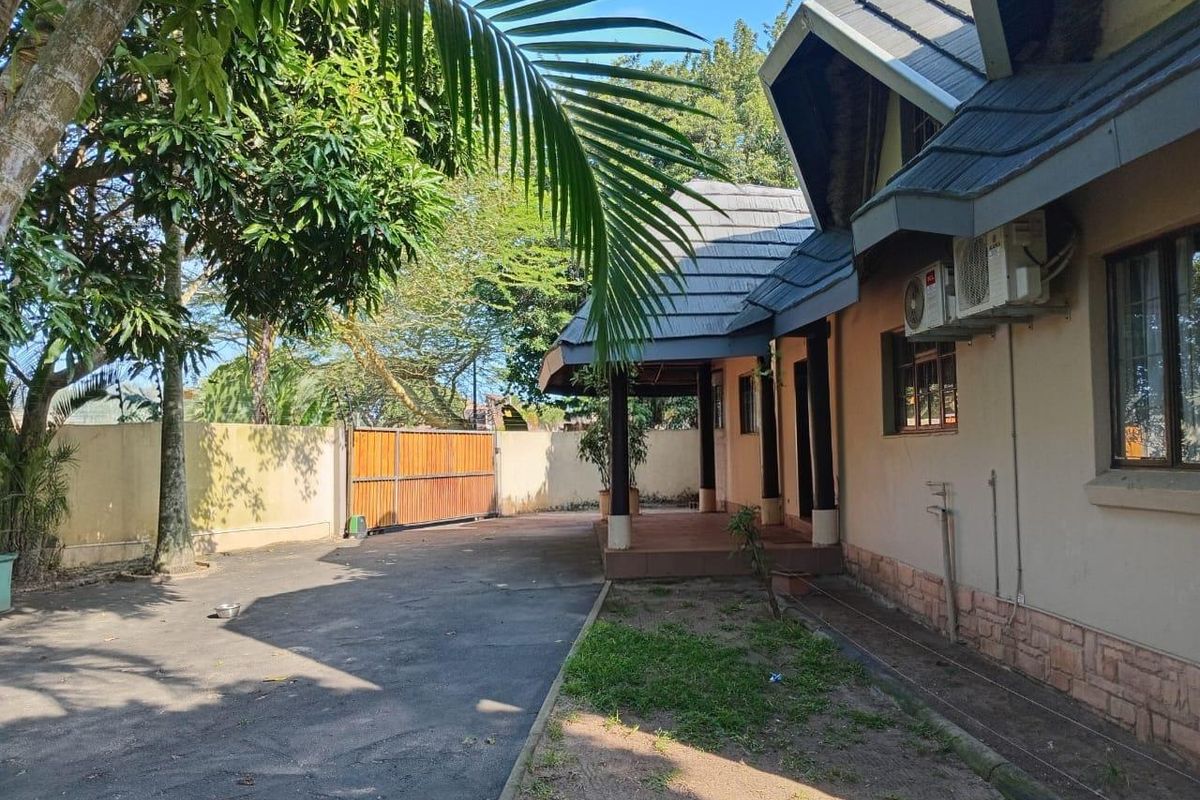 A view of the side exterior of the house featuring a covered patio, paved driveway, and perimeter boundary wall.