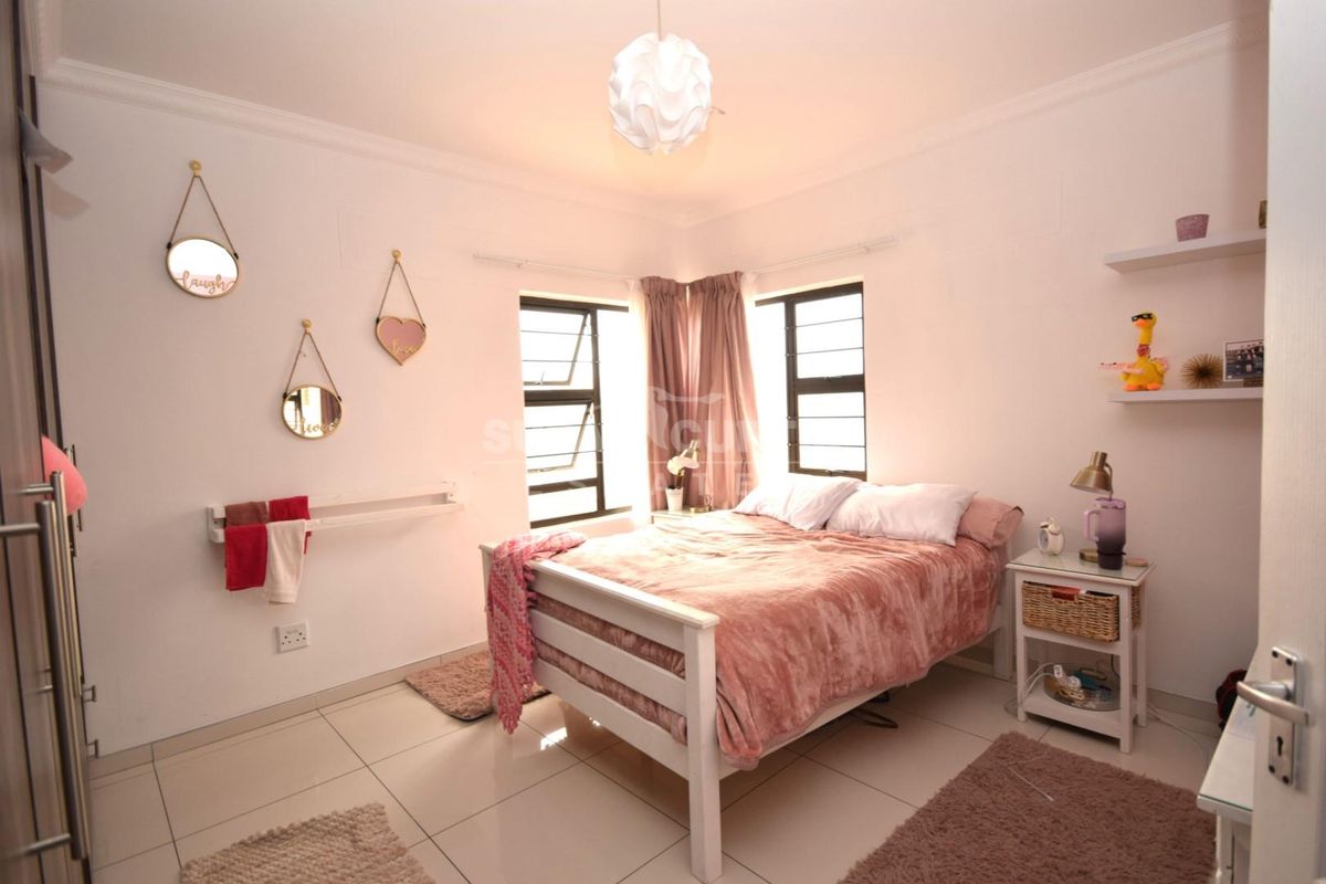 A well-lit bedroom featuring tiled flooring, built-in cupboards, and dual windows with security bars, providing a functional and comfortable living space.