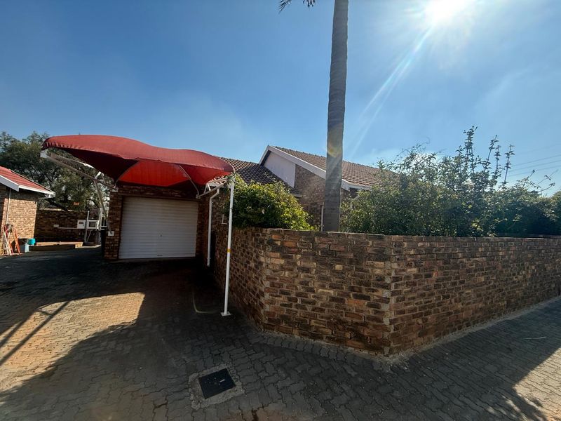 Front exterior view of the cluster property featuring a brick boundary wall, paved driveway, and a covered carport with a roller garage door.