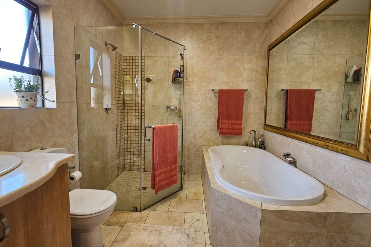 A well-maintained bathroom featuring a tiled walk-in shower, a built-in bathtub, a vanity with stone countertop, and a large wall-mounted mirror.