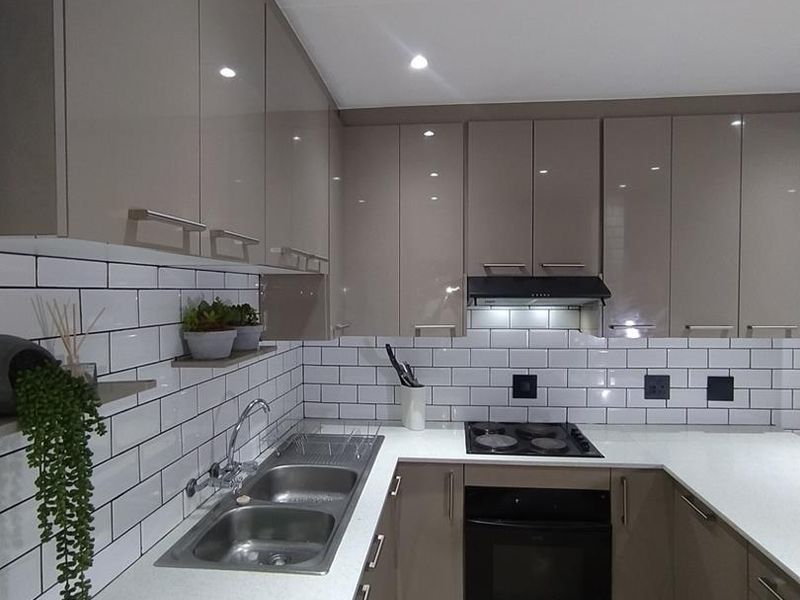 Modern kitchen featuring high-gloss cabinetry, white subway tile backsplash, quartz countertops, and integrated stainless steel appliances.