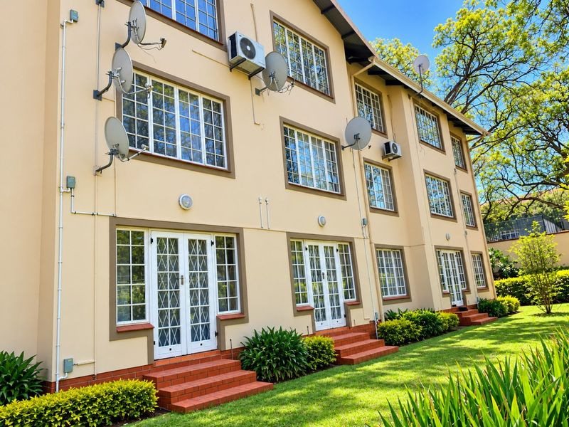 Rear elevation of a multi-story apartment building featuring brick entry steps, white grid-style french doors, and well-maintained landscaped garden areas.